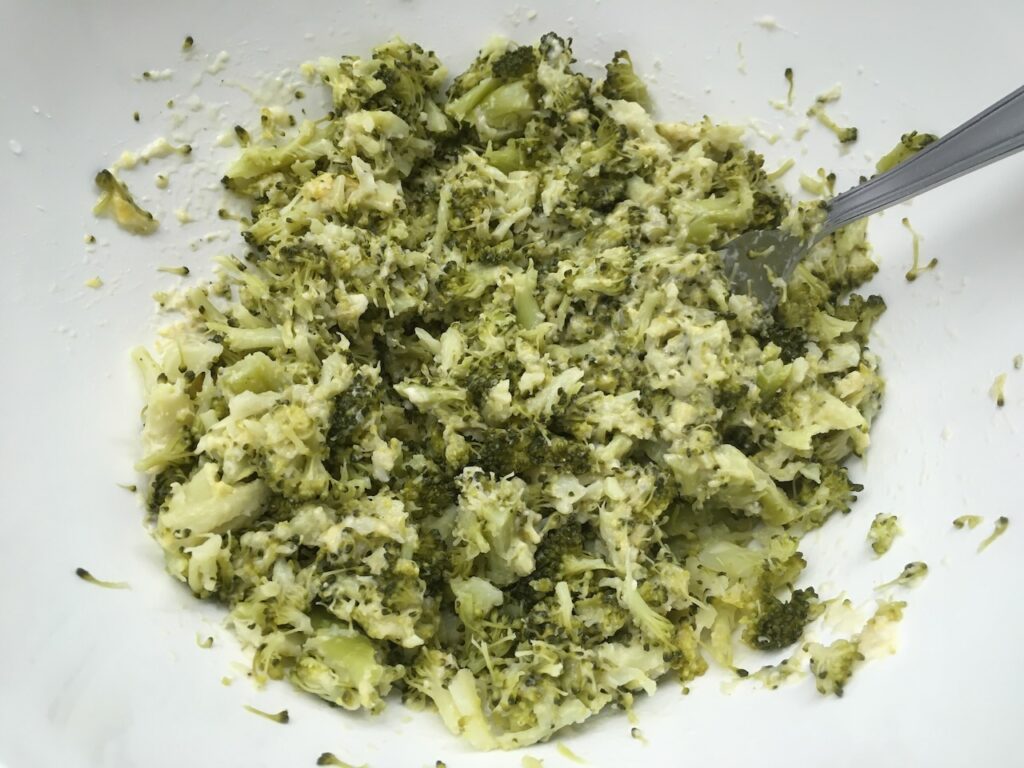 Recette galettes de brocoli au parmesan -Presser l'ail. Ajouter-le à la préparation ainsi que le brocolis. Ecraser le tout à l'aide d'une fourchette et mélanger.