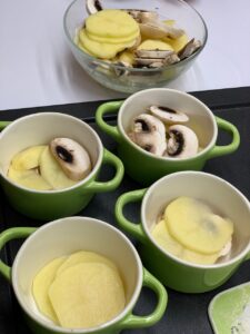 Recette mini gratins de pommes de terre champignons et épinards -Dans des petits cocottes, alterner des tranches de pommes de terre et de champignons.