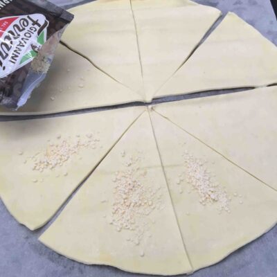 Recette minis croissants feuilletés à la coppa et au parmesan - Séparer les triangles de pâte et les parsemer individuellement de parmesan et poser une demi-tranche de coppa.