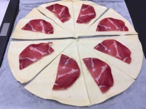 Recette minis croissants feuilletés à la coppa et au parmesan - Séparer les triangles de pâte et les parsemer individuellement de parmesan et poser une demi-tranche de coppa.