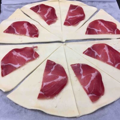 Recette minis croissants feuilletés à la coppa et au parmesan - Séparer les triangles de pâte et les parsemer individuellement de parmesan et poser une demi-tranche de coppa.