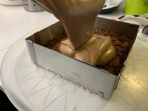 Recette Trianon - Verser la mousse au chocolat sur le croustillant en la répartissant bien aux 4 coins. Lisser la surface à l'aide d'une spatule. Réserver toute une nuit au réfrigérateur.