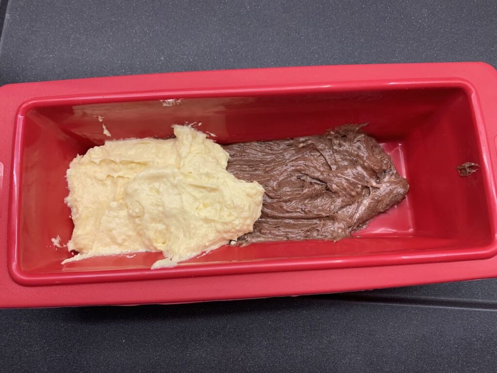 Recette quatre-quarts marbré au crumble de noisettes -Remplisser le moule en alternant une cuillère de pâte au chocolat avec une cuillère de pâte blanche.
Tracer un cercle dans la pâte avec le manche de la cuillère pour faire l'effet marbré.