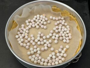 Recette tarte cookies aux pépites de chocolat et M&Ms -Après refroidissement, couvrir la pâte de papier cuisson et recouvrir de billes de cuisson. Ces billes permettent d'éviter que la pâte ne gonfle. Faire cuire au four à 170°C pendant 15 min.