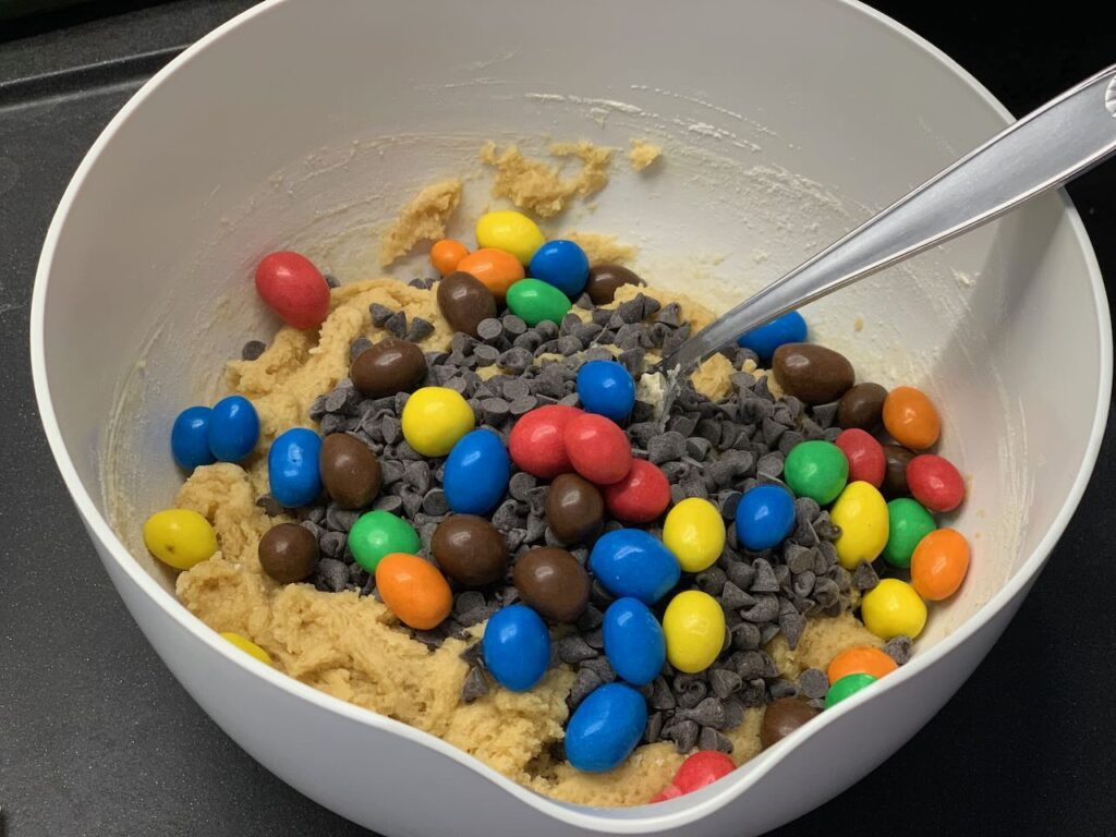 Recette tarte cookies aux pépites de chocolat et M&Ms -Ajouter les pépites de chocolat et les M&Ms et mélanger sans trop travailler la pâte.
