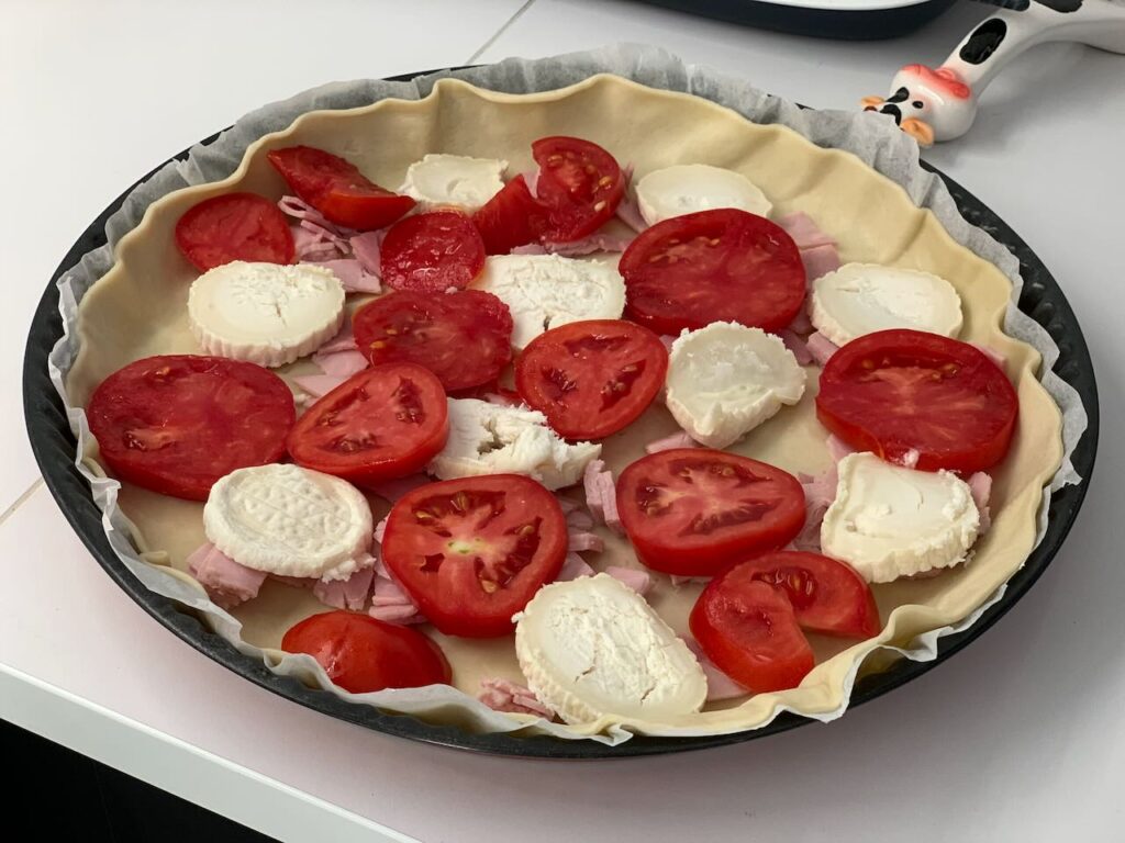 Recette quiche à la tomate, au jambon et au chèvre -Couper le jambon en dés et disposer sur le fond de tarte. Faire de même avec le chèvre.
Terminer en ajoutant les tomates coupées en tranches.